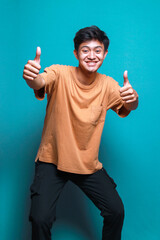 Casual asian man showing two thumbs up gesture and smiling to camera over blue background