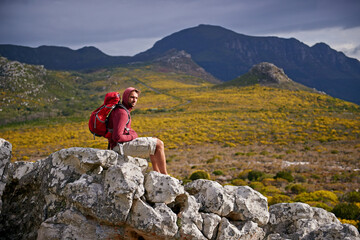 Man, rocks and relax on outdoor hike in nature, solitude and peace or calm on rocks for wellness. Male person, exercise and travel with backpack on vacation, adventure and explore bush for fitness
