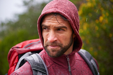 Nature, trekking and man with backpack in rain, hoodie and walking on landscape, fresh air and...