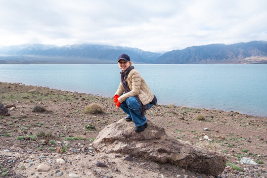 Blue lake and mountains. Travel scene, woman making a memorable funny photo. Bartogai reservoir, Almaty, Kazakhstan.
