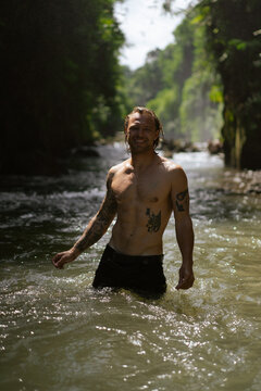 Young tattooed man at tropical waterfall, Bali island.