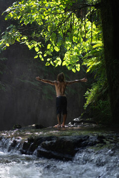 Young tattooed man at tropical waterfall, Bali island.