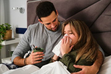 Husband taking care of his wife because she has flu on bed.