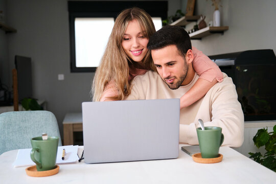 Man working at home while his wife is hugging him. - Powered by Adobe