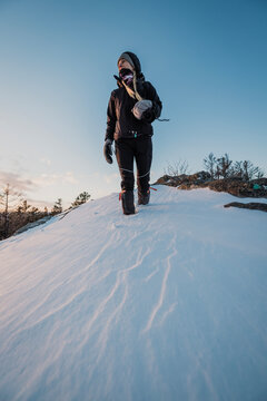 Female hiker walks walks through deep snow on cold winter day.