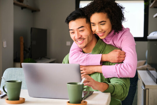 Multiethnic happy couple using the laptop and hugging.