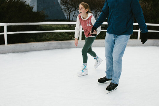 Daughter holds Dads hand while they ice skate together
