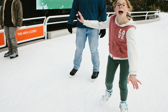 Tween girl ice skates with her father on ice path in winter
