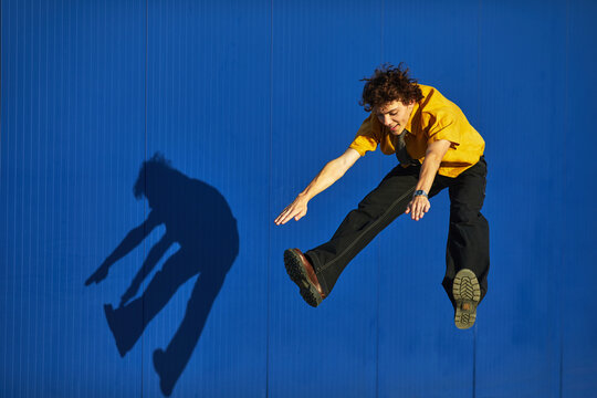 smiling young man in a yellow shirt jumping on a blue background