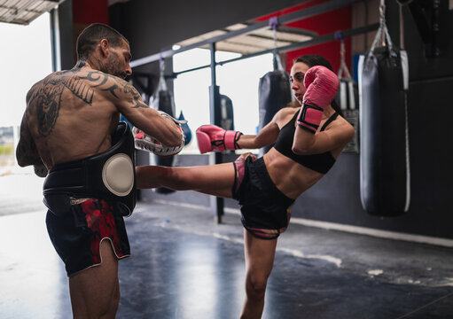 Female fighter practicing martial arts kicks with coach - Powered by Adobe