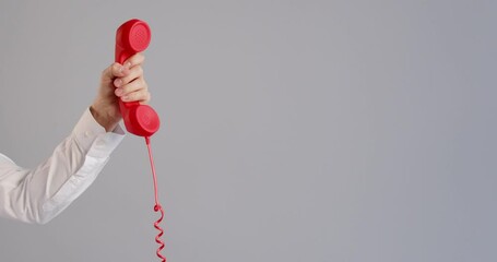 Man gets the phone, holds it for some time, then puts it down. Crop shot human hand holding red retro landline telephone receiver against a grey copy space background. Customer support hotline concept