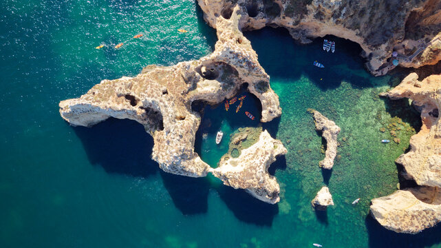 Aerial drone shot of kayaks and boats passing around magical Ponta da Piedade limestone cliffs. Exploring caves and tunnels of Lagos, Algarve, South of Portugal. Travel and adventure. Nomad life.