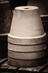 Black and white sepia toned image of a stack of clay flower pots on wooden bench in a Victorian...