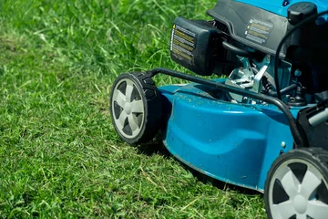 Gordijnen Lawn mower cutting grass. Small grass cuttings fly out of lawnmower. Grass clippings get spewed out of a mower pushed around by landscaper. CloseUp. Gardener working with mower machine. Mowing lawns © Marina Demidiuk