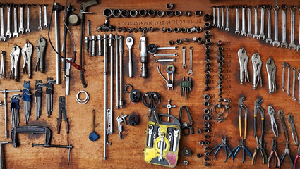 Many different sizes of tools, wrenches and pliers hanging on wooden panel background. Tool and...