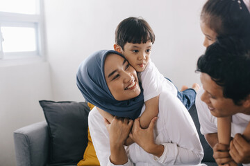 Cheerful Asian mom and dad piggy back their children while sitting on sofa in living room