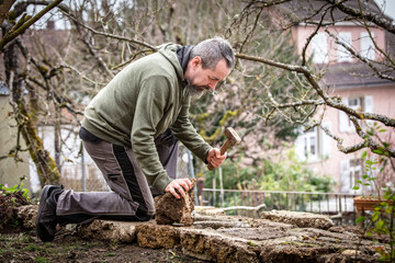 A male craftsman builds a raised bed or wall from rough stones