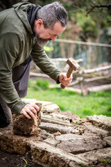 A male craftsman builds a raised bed or wall from rough stones