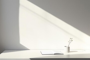 There is a notebook on a clean table. The background is a white wall that reflects the light. The atmosphere is quiet and contemplative. Minimalism with light shades and simple shapes.