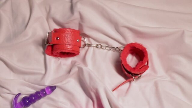 set of sex toys for masturbation and orgasm on a white sheet on the bed. Female vibrator, vacuum stimulator, butt plug and BDSM handcuffs