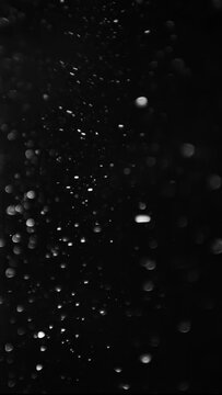 White dust swirling and falling slowly against a black background. Vertical video.