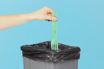 throw a plastic fork into the trash, disposable fork in hand in front of a trash can, plastic...