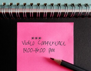 Pink note on notebook with text written Video Conference 14.00-16.00 pm, new normal work from home,...