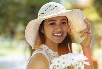Woman, portrait and flowers for relaxing in park or garden, smile and travel on summer holiday. Female person, peace and enjoy vacation in countryside, outdoors and hat on weekend adventure in nature
