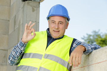 mature workman making ok sign on unfocused background