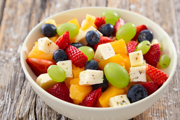 fruit salad. on a gray wooden table there is a small white plate with sliced fruits and feta cheese, top view, close up, fruit concept