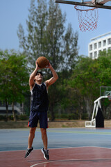 Full length of young sportsman jumping in basketball court and throwing ball to the basket