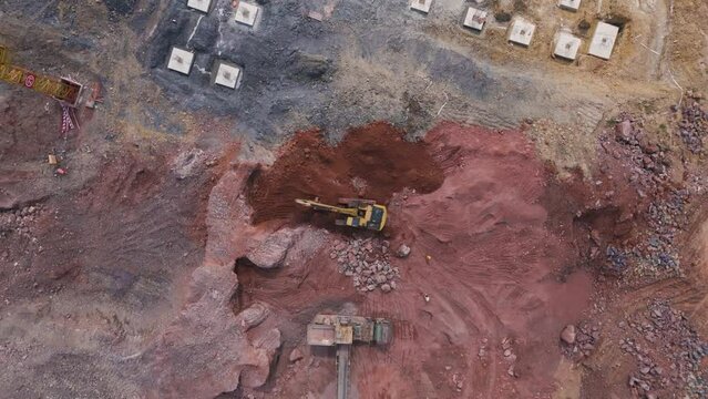 Aerial view of an excavator and crane loading crushed red rocks and sand. Trucks at work, construction site, multi-story construction, developer, preparing builders for construction, China