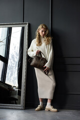 Obraz premium Studio portrait of beautiful woman with a curly blond hair holding brown bag, posing on gray background.