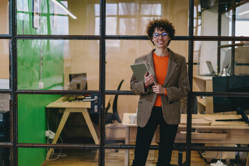 Fototapeta na wymiar Smiling woman in suit standing near glass wall in office