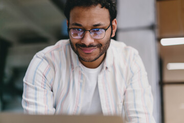 Happy bearded man in eyeglasses standing against blurred background in office