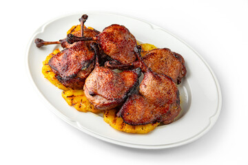 Grilled duck legs with crispy crust on a bed of grilled pineapples on a white plate. Banquet festive dishes. Gourmet restaurant menu. White background.