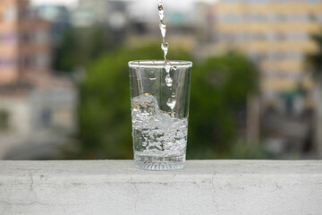 Pouring water into glass on an outdoor wall with natural blurred background. 
