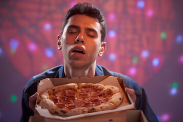 A young guy enjoys the smell of delicious pizza in a cardboard box