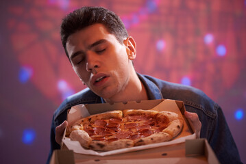 A young guy enjoys the smell of delicious pizza in a cardboard box
