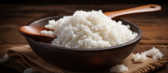 A staple food in many cuisines, a bowl of fluffy jasmine rice sits on a wooden table with a wooden...