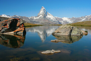 alpine landscape: mountain range with the pyramidal peak of the Matterhorn, reflected in the perfect mirror surface of the lake, Switzerland - obrazy, fototapety, plakaty