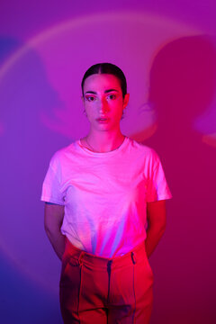 Young woman with hands behind back in neon lighting against gradient background