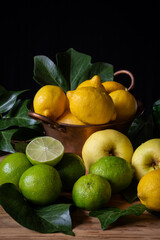 Closeup of scene with lemons, limes and yellow apples with green leaves on table, black background vertically, with copy space