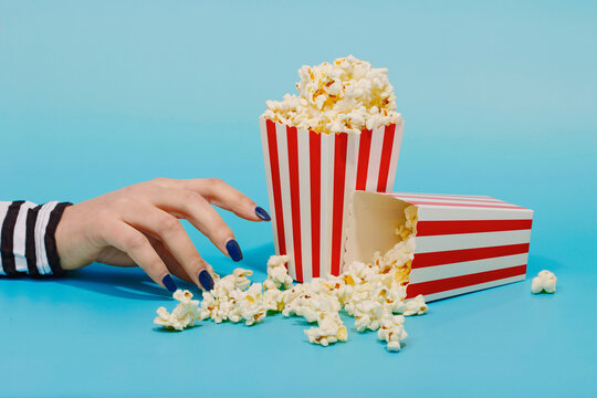Hand of woman reaching for popcorn over blue background