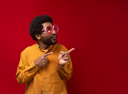 Man wearing party glasses and pointing against red background