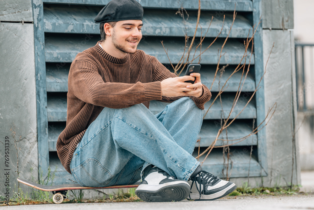 Wall mural young man sitting on the street with mobile phone chatting or playing online