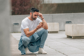 attractive young adult man with beard outdoors looking worried at mobile phone
