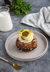A French cream puff crack bun (Choux au Craquelin) in a plate, topped with cream pistachio and its grains with spoon and milk pot. It's a dessert base of savory choux dough bun 