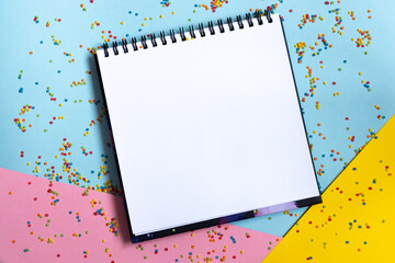 Mock up of empty spiral scketchbook with white paper on bright vibrant background with colorful confetti . Copy space. - obrazy, fototapety, plakaty