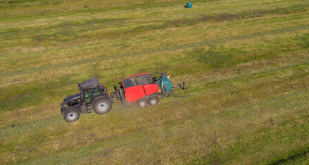 Schwarzer Treker oder Traktor mit einer roten Stroh Festkammerpresse bei der Strohernte auf einem gemähten Feld - obrazy, fototapety, plakaty